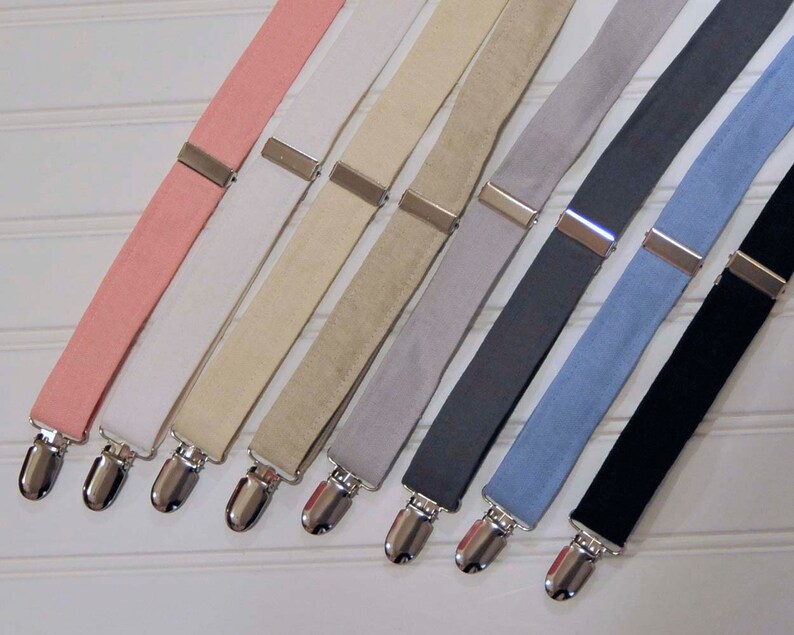 May include: Eight pairs of suspenders in different colors, including pink, white, beige, gray, dark gray, light blue, and black. The suspenders have silver clips.