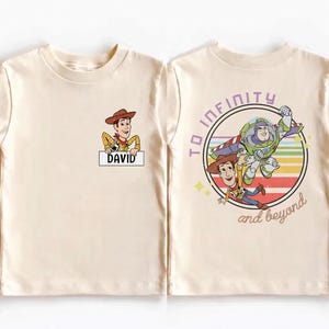 Peut inclure: T-shirt cr&egrave;me avec une image de dessin anim&eacute; de Woody de Toy Story tenant une pancarte avec le nom "DAVID". Le dos du t-shirt pr&eacute;sente un graphisme circulaire avec Buzz l'&Eacute;clair, Woody et le texte "TO INFINITY and beyond".