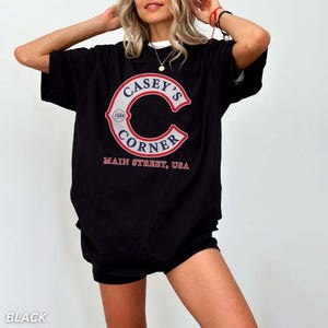May include: Black t-shirt with a white collar featuring a large red and white graphic of "Casey's Corner" with "Main Street, USA" printed below. The graphic includes a large "C" shape with the text inside. The year "1888" is also included.