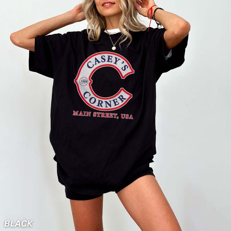 May include: Black t-shirt with a white collar featuring a large red and white graphic of "Casey's Corner" with "Main Street, USA" printed below. The graphic includes a large "C" shape with the text inside. The year "1888" is also included.