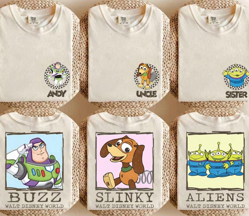Puede incluir: Seis camisetas color crema con personajes de Toy Story de Disney. Las camisetas presentan a Buzz Lightyear, Slinky Dog y los Aliens, con textos como "ANDY", "UNCLE", "SISTER", "BUZZ", "SLINKY" y "ALIENS".