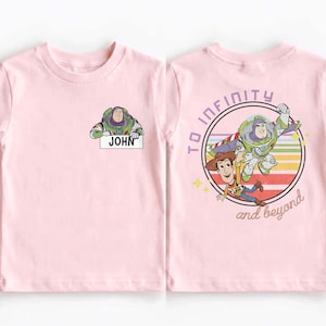 Peut inclure: T-shirt rose clair avec Buzz l'&Eacute;clair tenant une pancarte "JOHN". Au dos, un motif circulaire avec Buzz l'&Eacute;clair, Woody et l'inscription "TO INFINITY and beyond".