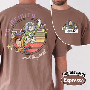 Peut inclure: T-shirt couleur expresso avec un motif de Buzz l'&Eacute;clair et Woody de Toy Story, avec le texte "To Infinity and Beyond". Une petite image de Buzz l'&Eacute;clair avec le nom "JOHN" est sur le devant. Le t-shirt est &eacute;tiquet&eacute; "COMFORT COLOR".