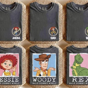 Puede incluir: Seis camisetas de color gris oscuro con dise&ntilde;os de personajes de Toy Story. Las camisetas presentan personajes como Jessie, Woody y Rex, junto con los textos "MOM", "DAD" y "BABY". Cada camiseta tiene el texto "WALT DISNEY WORLD" debajo de la imagen del personaje.