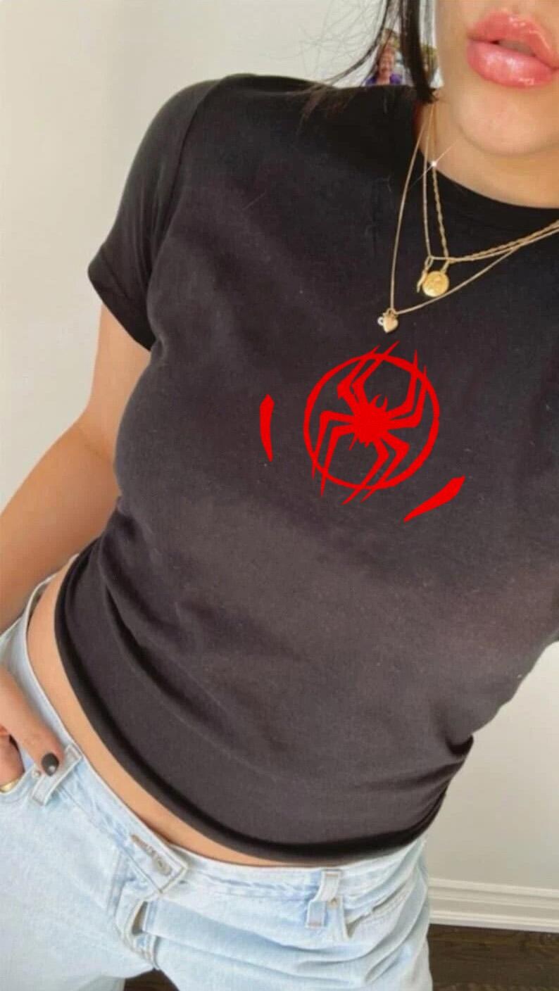 Puede incluir: Camiseta negra con un gr&aacute;fico de ara&ntilde;a roja en un c&iacute;rculo. La camiseta de manga corta est&aacute; hecha de un material suave. El gr&aacute;fico es un dise&ntilde;o de ara&ntilde;a estilizado. La camiseta se combina con vaqueros azul claro.