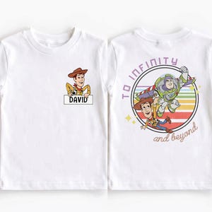 Peut inclure: T-shirt blanc avec une image de dessin anim&eacute; de Woody de Toy Story, avec le nom "DAVID" sur un panneau. Le dos du t-shirt pr&eacute;sente un motif circulaire avec Buzz Lightyear, Woody et le texte "TO INFINITY and beyond".