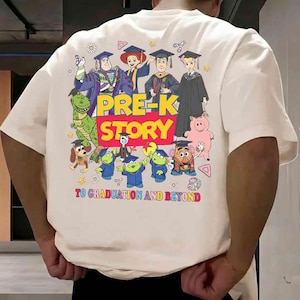 K&ouml;nnte beinhalten: Cremefarbenes T-Shirt mit einem farbenfrohen Grafikdesign von Zeichentrickfiguren in Abschlusskleidung. Der Text "PRE-K STORY" ist prominent dargestellt, mit dem Satz "TO GRADUATION AND BEYOND" darunter. Das Design umfasst verschiedene Cartoonfiguren.