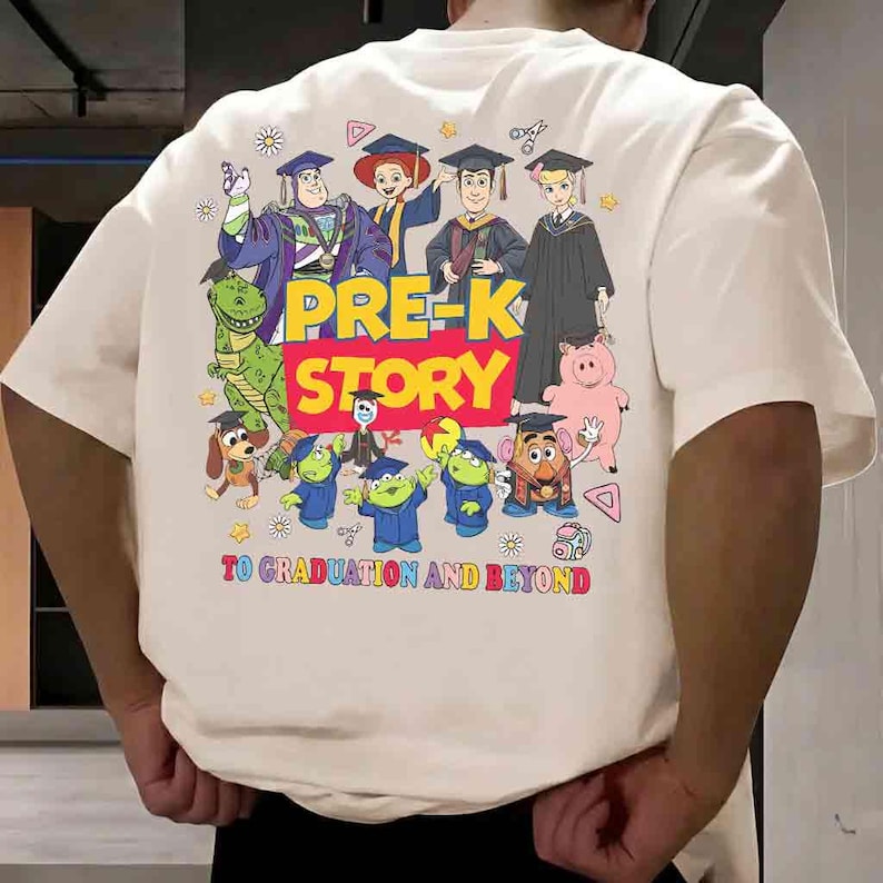 K&ouml;nnte beinhalten: Cremefarbenes T-Shirt mit einem farbenfrohen Grafikdesign von Zeichentrickfiguren in Abschlusskleidung. Der Text "PRE-K STORY" ist prominent dargestellt, mit dem Satz "TO GRADUATION AND BEYOND" darunter. Das Design umfasst verschiedene Cartoonfiguren.