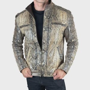 May include: A snakeskin-patterned leather jacket with a zip-up front and a stand-up collar. The jacket features two chest pockets with zippers and a brown interior lining. The sleeves have a quilted design.