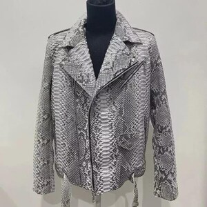 Può includere: Giacca in pelle grigia e bianca con motivo a pelle di serpente, in classico stile biker. La giacca presenta un colletto a lancia, chiusura asimmetrica con zip e cintura in vita. La giacca è esposta su un manichino.