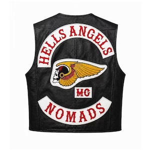 May include: A black leather vest featuring a large embroidered patch on the back. The patch displays the text HELLS ANGELS in red on a white curved background, a winged skull emblem in yellow and red, the letters MG, and the word NOMADS in red.