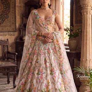 Peut inclure: Un lehenga choli blanc orné de broderies florales multicolores dans des tons de rose, jaune, bleu et vert, rehaussé de fils métalliques dorés. L'ensemble comprend une dupatta transparente assortie avec des bords festonnés.