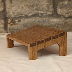 May include: A wooden stand with a natural wood finish and a unique design featuring a series of inset wood pieces. The stand has a rectangular top and four legs.