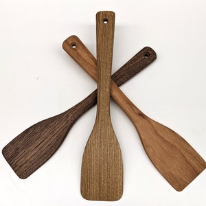 May include: Three wooden kitchen spatulas, one dark brown, one light brown, and one medium brown, are arranged in an X shape.