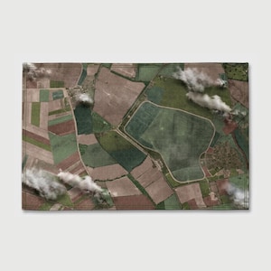 May include: A rectangular area rug featuring an aerial satellite view of agricultural farmland. The design displays a patchwork of brown, green, and tan fields separated by roads and paths, with scattered white clouds partially obscuring the landscape.