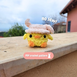 Pode incluir: Um pintinho amarelo de crochê feito à mão, com pés laranja e um chapéu rosa claro. O pintinho tem olhos pretos. O texto na imagem diz "no sew!" e "PDF crochet pattern".