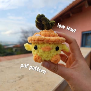 Pode incluir: Um cogumelo de crochê amarelo e laranja com um topo verde. O cogumelo tem olhos pretos e um bico laranja. Os textos "low sew!" e "pdf pattern" são visíveis.
