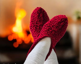 May include: A cozy scene featuring red knitted slippers over white socks, with a warm fireplace in the background. The slippers are a vibrant red, and the socks are a soft white. The focus is on comfort and relaxation.