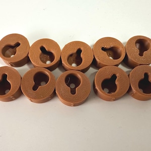 May include: Ten small, round, brown plastic components arranged in two rows of five. Each piece features a textured surface and a central keyhole-shaped opening designed for mounting, with a circular hole at the bottom and a narrow slot extending upward.