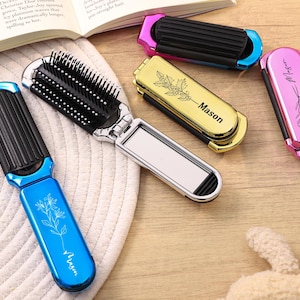 May include: Several folding hairbrushes in blue, gold, and pink are displayed. Each brush has a mirror and a comb. The blue brush has a floral design and the name "Mason" printed on it. The gold brush also has the name "Mason" printed on it.