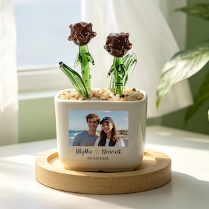 Könnte beinhalten: Ein weißer Keramiktopf mit zwei Glasrosen-Skulpturen. Der Topf zeigt ein Foto eines Paares mit den Namen "Blythe & Bennett" und dem Datum "09/15/2026". Der Topf steht auf einem Holztablett.