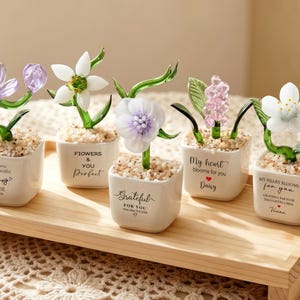 May include: Five small glass flowers in white ceramic pots filled with pebbles. Each pot features unique text: Thank you for the beautiful flowers Chloe, Flowers & You Perfect, Grateful For You, My heart blooms for you Daisy, and My heart blooms for you Vivian.