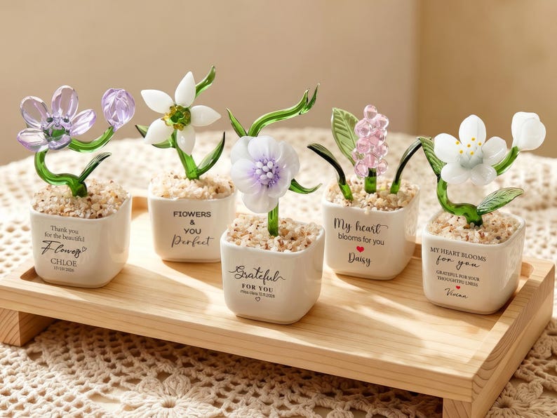 May include: Five small glass flowers in white ceramic pots filled with pebbles. Each pot features unique text: Thank you for the beautiful flowers Chloe, Flowers & You Perfect, Grateful For You, My heart blooms for you Daisy, and My heart blooms for you Vivian.