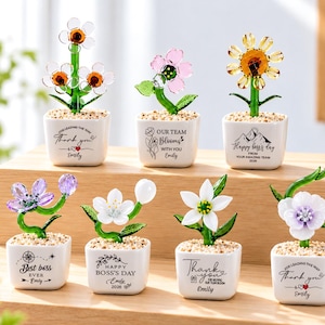 Peut inclure: Sept petites figurines de fleurs en verre dans des pots en céramique carrés blancs remplis de cailloux. Chaque pot présente du texte et des graphiques imprimés en noir, incluant des phrases comme Thank You, Best Boss Ever et Happy Boss's Day.
