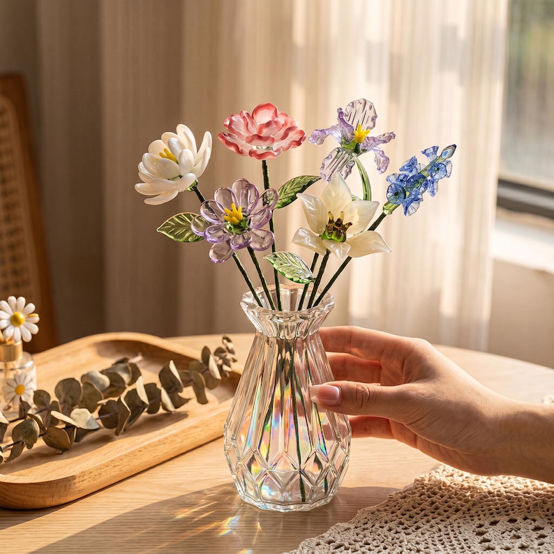 May include: A clear glass vase with a diamond pattern holds a bouquet of colorful glass flowers. The flowers include white, pink, purple, and blue blooms with green leaves. The vase sits on a wooden tray.