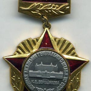 May include: A gold-coloured military medal with a red star and a central medallion bearing Cyrillic text and a building illustration. The medal includes a ribbon bar with three small emblems.