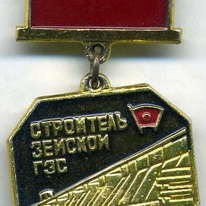 Puede incluir: Medalla dorada vintage con una parte superior rectangular de esmalte rojo y un colgante octogonal. El colgante presenta texto cirílico, un emblema de bandera roja y una ilustración detallada en oro de un edificio. Un pequeño anillo conecta las dos partes.
