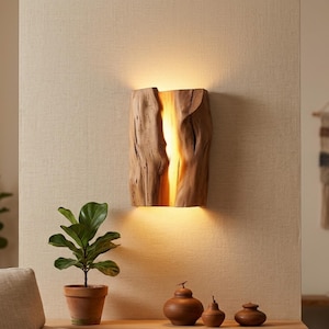 Puede incluir: Aplique de pared rústico de madera con un brillo cálido y acogedor. La lámpara está hecha de un trozo de madera natural, con un centro tallado que emite una luz suave y dorada. El aplique está montado en una pared beige.