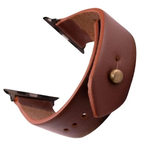 Op de afbeelding: Een bruin leren horlogebandje met een gebogen ontwerp. De band heeft een messingkleurige knoopsluiting en is ontworpen voor een smartwatch. De band is gemaakt van glad, duurzaam leer.