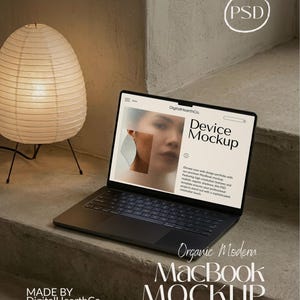 May include: A black MacBook laptop with a screen displaying a device mockup. The laptop is on a concrete surface, next to a paper lantern lamp. The text on the screen reads "Device Mockup". The text "Organic Modern MacBook Mockup" is also visible.