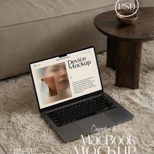 Puede incluir: Un ordenador portátil MacBook gris con un teclado negro está abierto sobre una alfombra suave de color blanquecino. La pantalla muestra una maqueta de dispositivo con el texto "Device Mockup". Las palabras "Organic Modern MacBook Mockup" están debajo. Una pequeña mesa de madera y un sofá beige están en el fondo.
