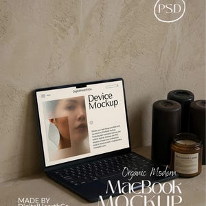 May include: A dark blue MacBook laptop with a screen displaying a website mockup. The mockup features a woman's face and text. Beside the laptop are black candles and a scented candle in a glass jar. The text on the image says "Organic Modern MacBook Mockup".