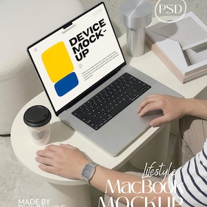 May include: A silver laptop displaying a screen with the text DEVICE MOCK-UP, a yellow rectangle, and a blue rectangle. The laptop is on a white table next to a white coffee cup with a black lid, a silver cylindrical object, and a stack of papers.