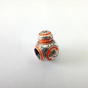May include: A silver and orange charm with a spherical design. The charm features a detailed design with orange enamel accents and the word "PANDORA" engraved on the top. The charm is a collectible item.