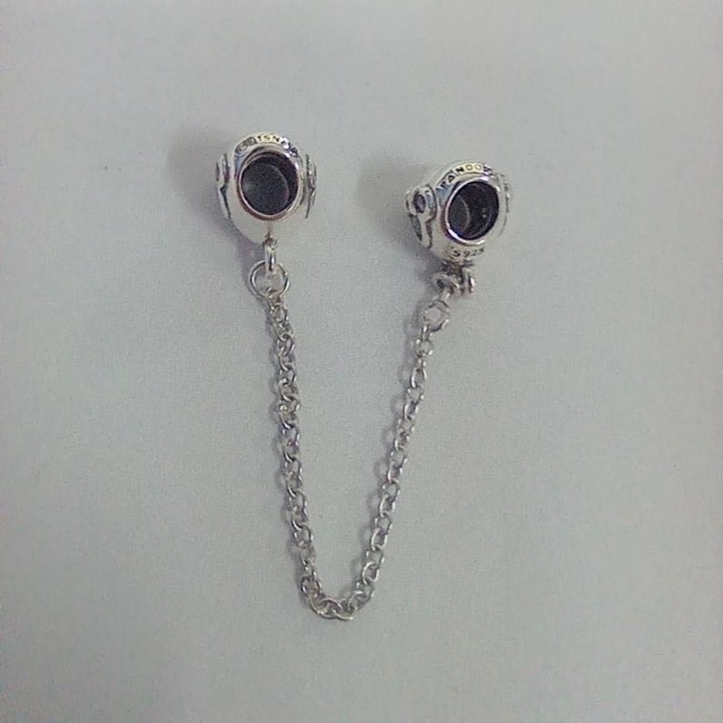 Op de afbeelding: Een zilveren veiligheidsketting voor een bedelarmband met twee ronde bedels. Elke bedel heeft een donker centrum en is verbonden door een fijne ketting. De bedels hebben een gedetailleerd ontwerp.