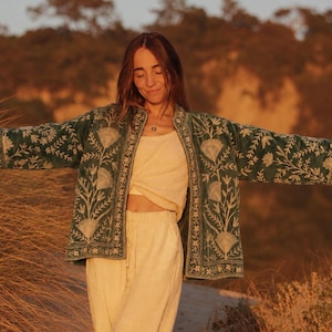 May include: A dark green open-front jacket featuring cream-colored floral embroidery on the sleeves and front panels, worn over a cream-colored top and matching cream-colored drawstring trousers with a relaxed fit and straight leg design.