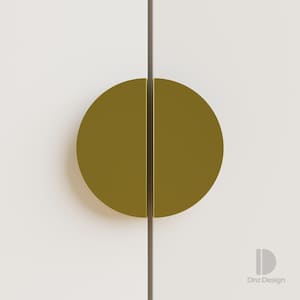 Op de afbeelding: Close-up van een paar olijfgroene, halfronde kastgrepen die een volledige cirkel vormen. De grepen zijn gemonteerd op een witte kastdeur met een donkerbruine verticale lijn ertussen. Het ontwerp is modern en minimalistisch.