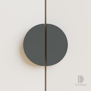 Puede incluir: Primer plano de una puerta de armario blanca con un tirador semicircular gris oscuro. El tirador está dividido por la mitad, con cada mitad a cada lado de la costura de la puerta. Diseño minimalista.