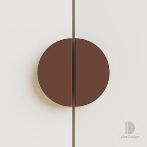 May include: A close-up of a cabinet door with a brown, semi-circular handle. The handle is split in half by a vertical line. The cabinet door is white. The design is minimalist and modern.