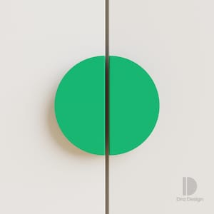 Può includere: Primo piano di un'anta di armadio con una maniglia semicircolare verde brillante. La maniglia è divisa a metà da una linea verticale e l'anta è di colore beige chiaro. Il design è moderno e minimalista.