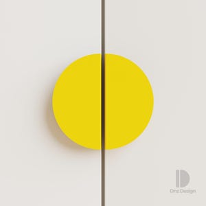 Könnte beinhalten: Nahaufnahme einer Schranktür mit einem leuchtend gelben, halbkreisförmigen Griff. Der Griff wird durch eine dunkelbraune vertikale Linie geteilt. Die Schranktür hat eine neutrale, cremeweiße Farbe. Das Design ist modern und minimalistisch.