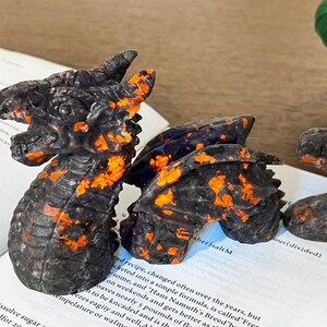 May include: A detailed, black and orange dragon figurine with a textured surface. The dragon is posed on a book with visible text. The figurine's design includes scales and a detailed head.
