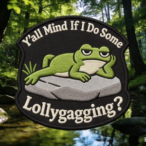 May include: Embroidered patch featuring a green frog resting on a gray rock. The patch has the text "Y'all Mind If I Do Some Lollygagging?" in white lettering on a black background. The patch is surrounded by a black border.