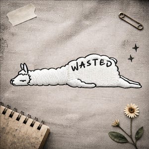 Könnte beinhalten: Gestickter weißer Lama-Aufnäher mit dem Wort „WASTED“ in Schwarz. Das Lama liegt mit geschlossenen Augen. Der Aufnäher befindet sich auf einem strukturierten, neutral getönten Hintergrund.