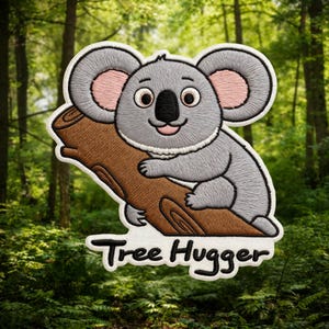 Puede incluir: Parche bordado con un koala gris abrazando una rama marrón. El koala tiene orejas internas rosas y una nariz negra. El texto "Tree Hugger" está debajo del koala en escritura negra. El parche tiene un borde blanco.
