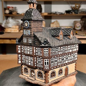 Può includere: Modello in ceramica dettagliato di un edificio europeo tradizionale, con un campanile e molte finestre. La struttura è dipinta in marrone, beige e bianco, con un tetto strutturato e intricati dettagli architettonici.